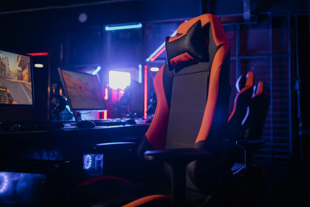 Modern gaming setup featuring a sleek chair and powerful PCs under neon lights.